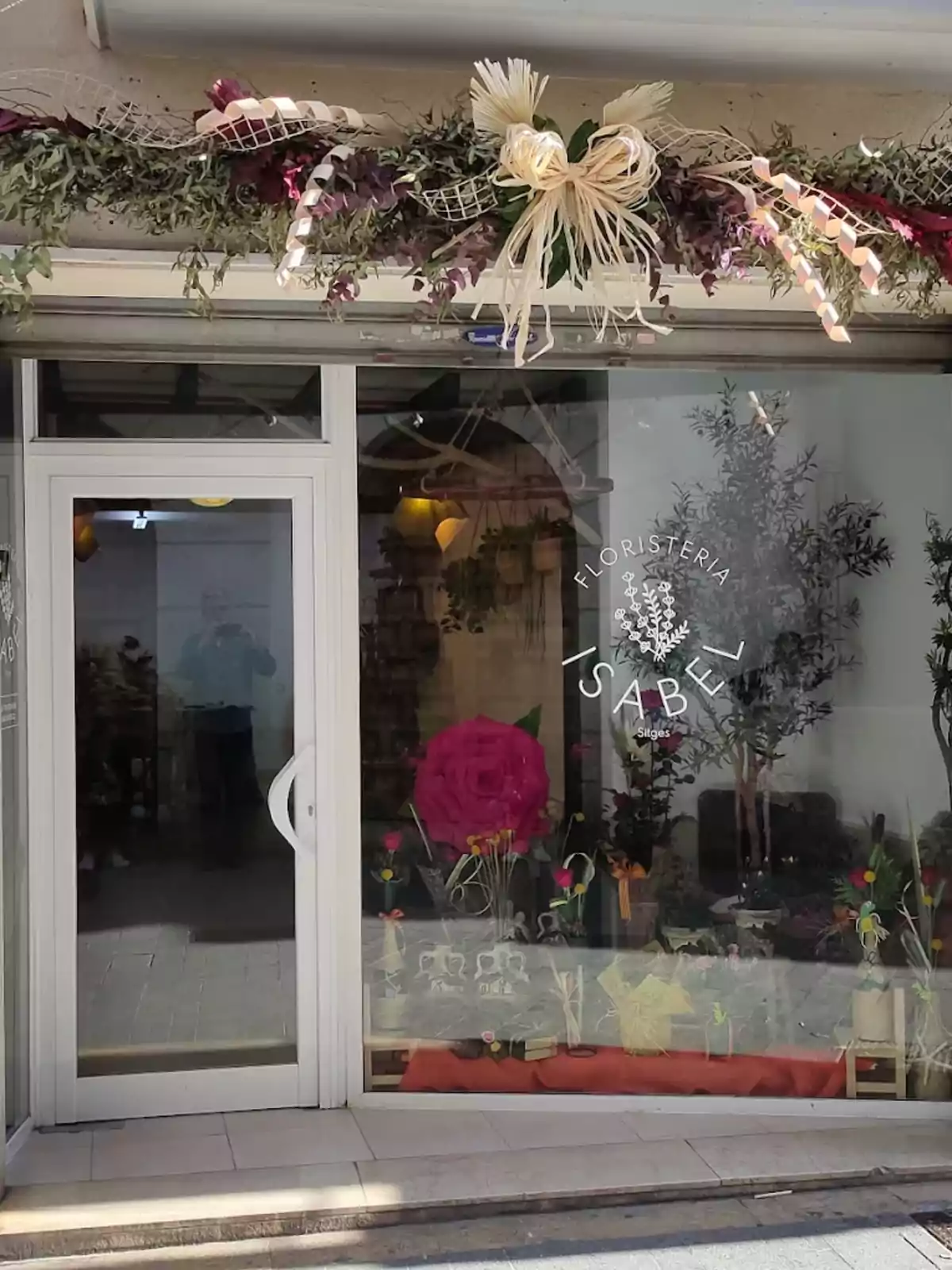 Fachada de una floristería con un gran lazo decorativo y arreglos florales en la entrada y el escaparate Fachada de una floristería con un gran lazo decorativo y arreglos florales en la entrada y el escaparate