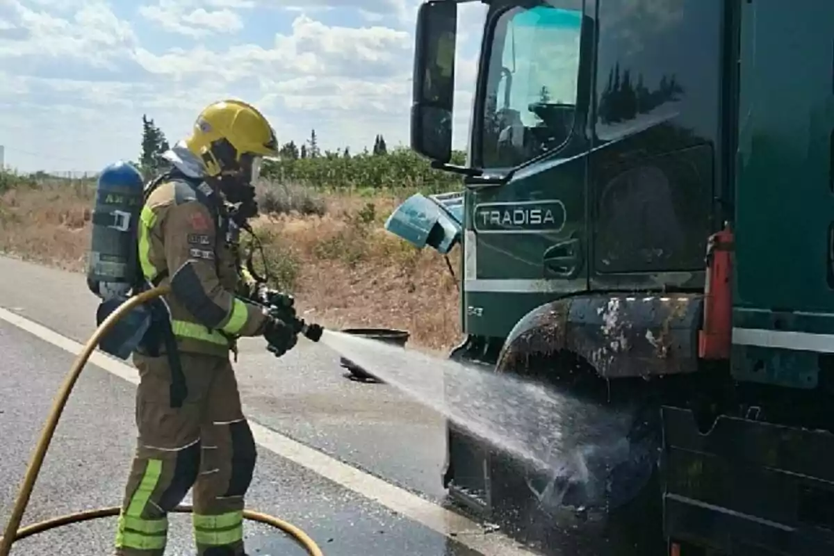 Un bomber apaga un incendi a la part davantera d’un camió verd en una carretera