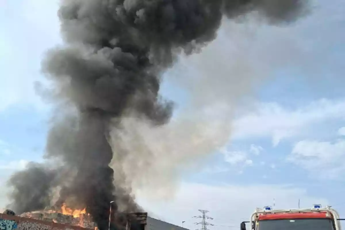 Incendio con grandes columnas de humo negro y un camión de bomberos en primer plano bajo un cielo parcialmente nublado