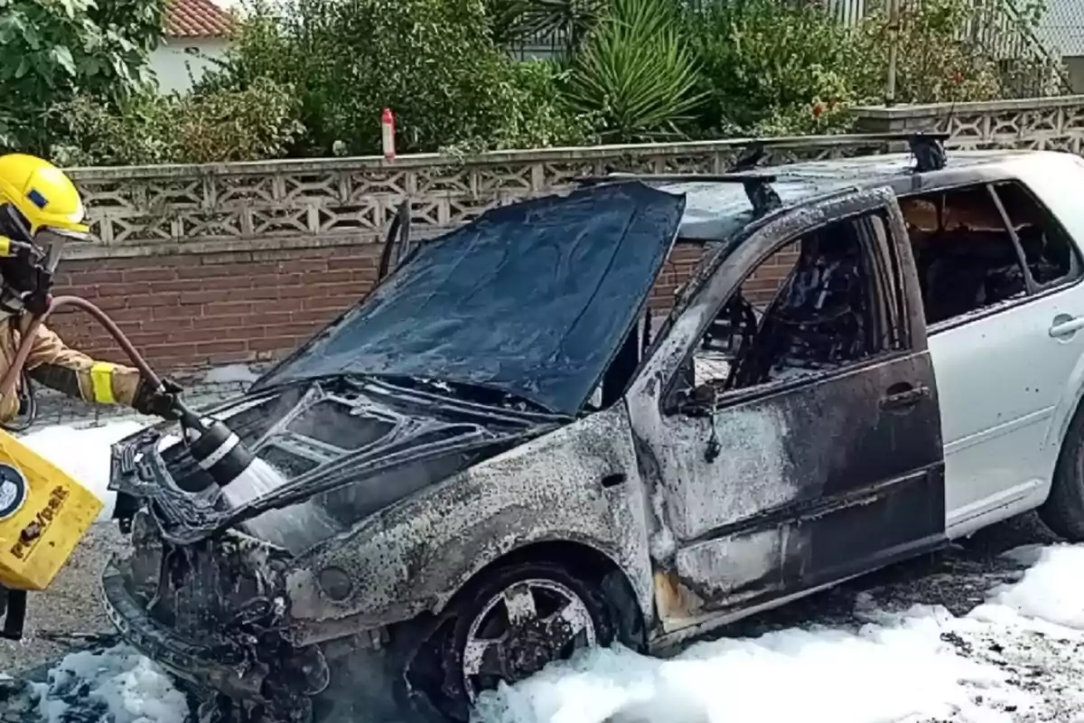 Un bomber apaga l’incendi d’un cotxe cremat amb escuma en un carrer residencial