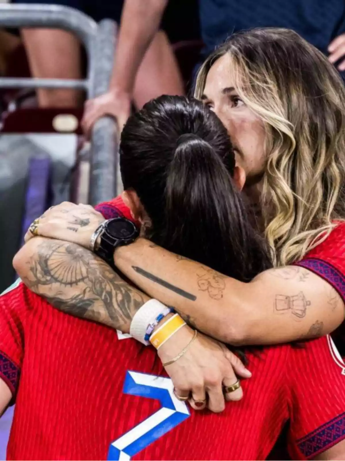Dos mujeres con camisetas rojas se abrazan con fuerza mostrando tatuajes en los brazos y una expresión de emoción Dos mujeres con camisetas rojas se abrazan con fuerza mostrando tatuajes en los brazos y una expresión de emoción