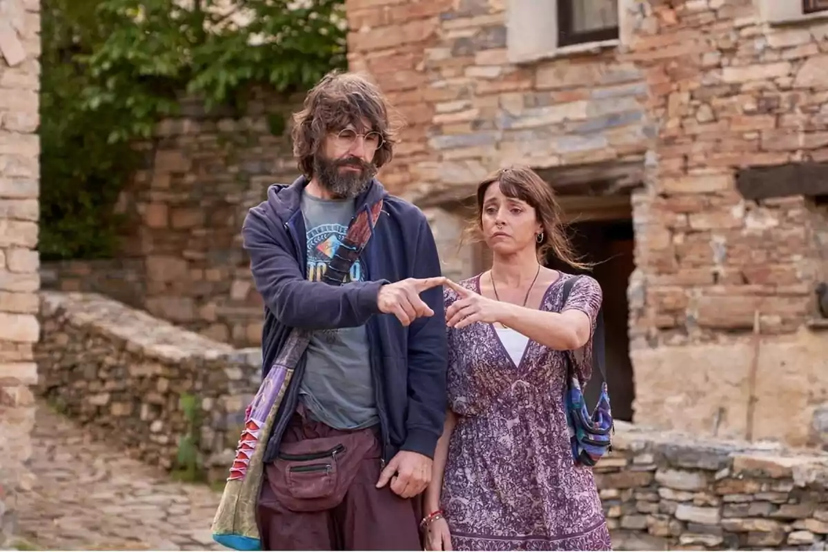 Dues persones dretes en un carrer empedrat assenyalant cap al mateix punt amb una expressió seriosa davant d’una paret de pedra antiga Dues persones dretes en un carrer empedrat assenyalant cap al mateix punt amb una expressió seriosa davant d’una paret de pedra antiga