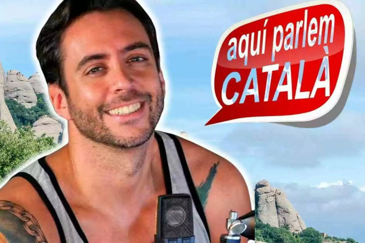 Hombre sonriente con barba y tatuaje en el brazo frente a un paisaje montañoso y un cartel que dice aquí parlem català