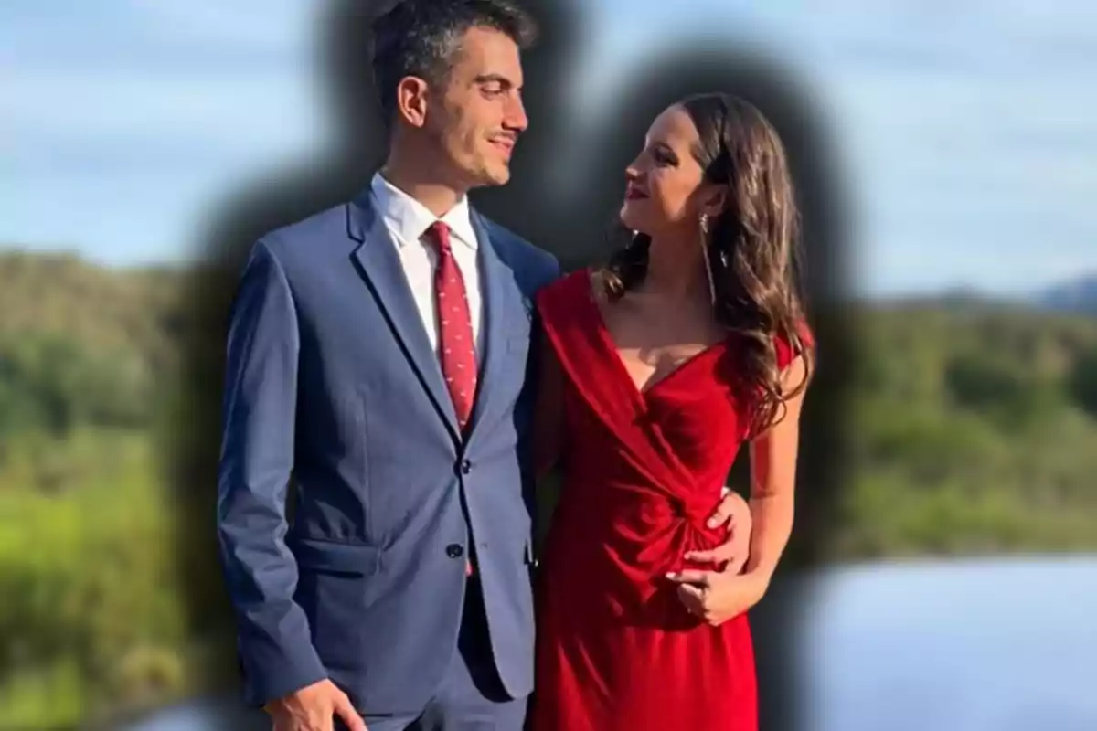 Parella elegantament vestida es mira amb afecte a l’aire lliure, ell porta un vestit blau i corbata vermella, ella porta un vestit vermell.