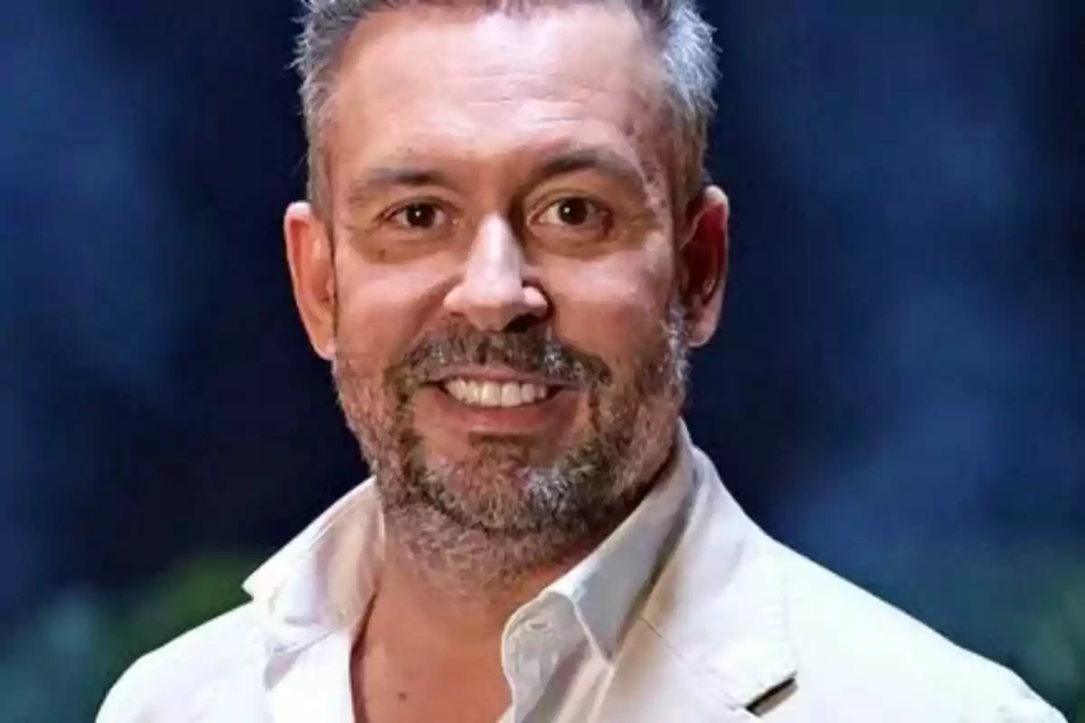 Kike Calleja de cabell curt i canós amb barba i bigoti, somrient, vestit amb americana clara i camisa blanca, fons fosc desenfocat a Supervivientes All Stars Kike Calleja de cabell curt i canós amb barba i bigoti, somrient, vestit amb americana clara i camisa blanca, fons fosc desenfocat a Supervivientes All Stars