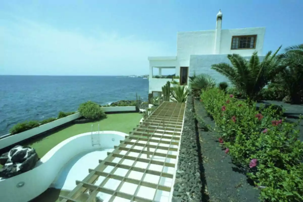 Casa blanca moderna junto al mar con piscina vacía, jardín con palmeras y flores, y una pérgola de madera Casa blanca moderna junto al mar con piscina vacía, jardín con palmeras y flores, y una pérgola de madera