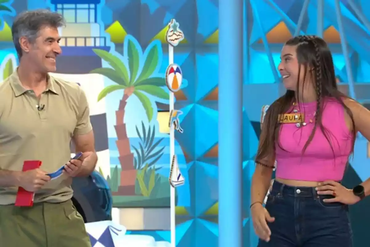 Jorge Fernández y Laura sonríen mientras participan en un programa de televisión con decoración colorida y temática veraniega. Captura de 'La Ruleta de la Suerte' Jorge Fernández y Laura sonríen mientras participan en un programa de televisión con decoración colorida y temática veraniega. Captura de 'La Ruleta de la Suerte'