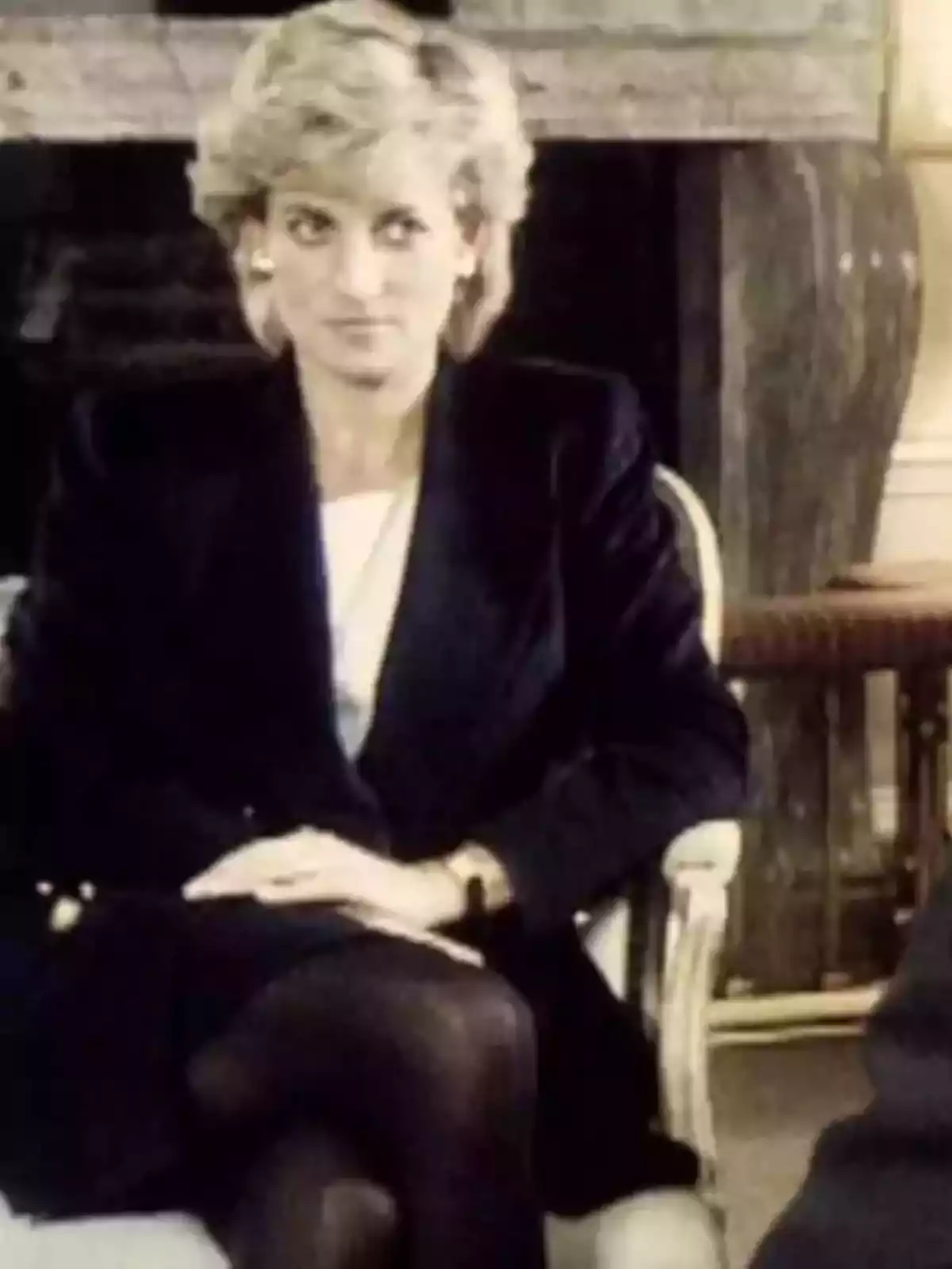 Mujer sentada con expresión seria usando un saco oscuro y medias negras en una sala elegante Mujer sentada con expresión seria usando un saco oscuro y medias negras en una sala elegante