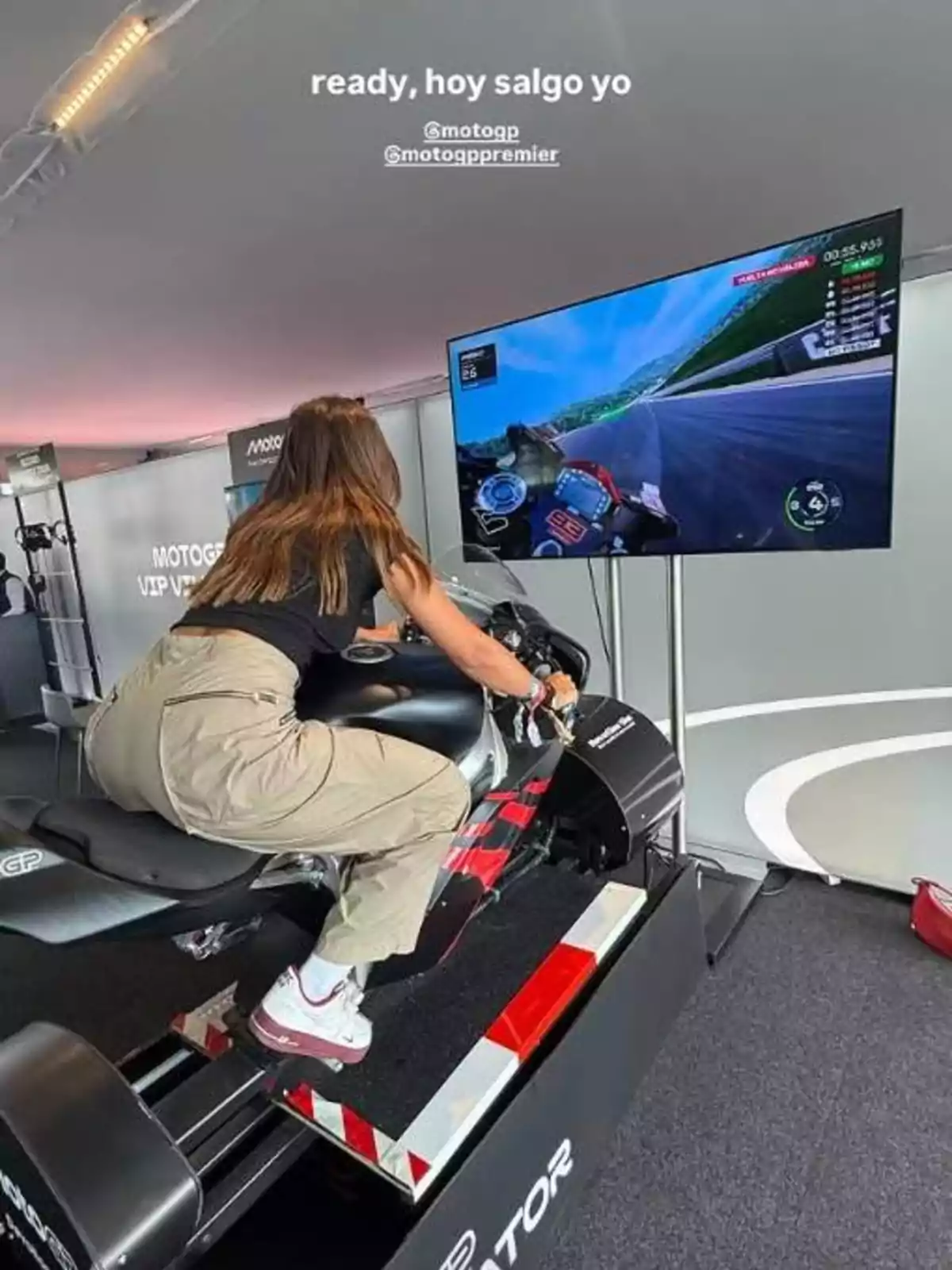 Dona jugant en un simulador de motocicleta davant d’una pantalla gran que mostra una cursa virtual Dona jugant en un simulador de motocicleta davant d’una pantalla gran que mostra una cursa virtual