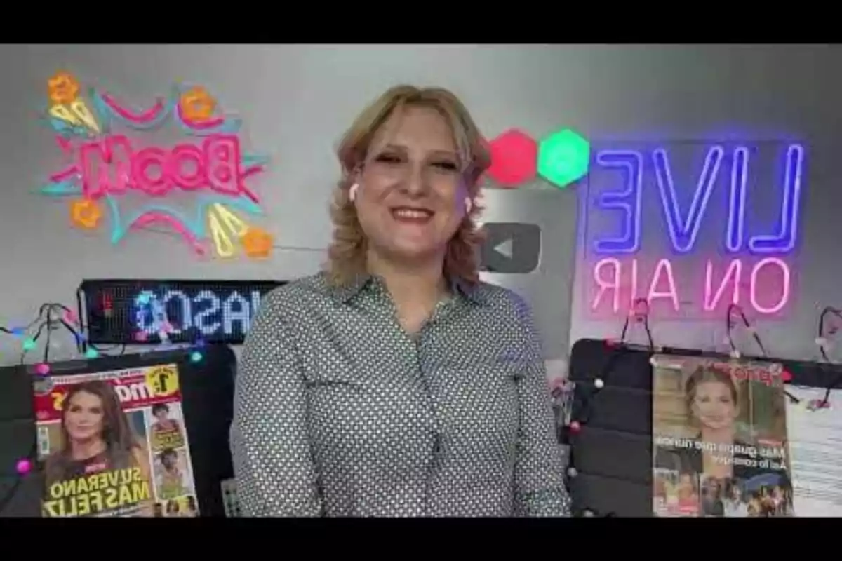 Persona sonriente con camisa de puntos frente a una pared decorada con letreros de neón y revistas Persona sonriente con camisa de puntos frente a una pared decorada con letreros de neón y revistas