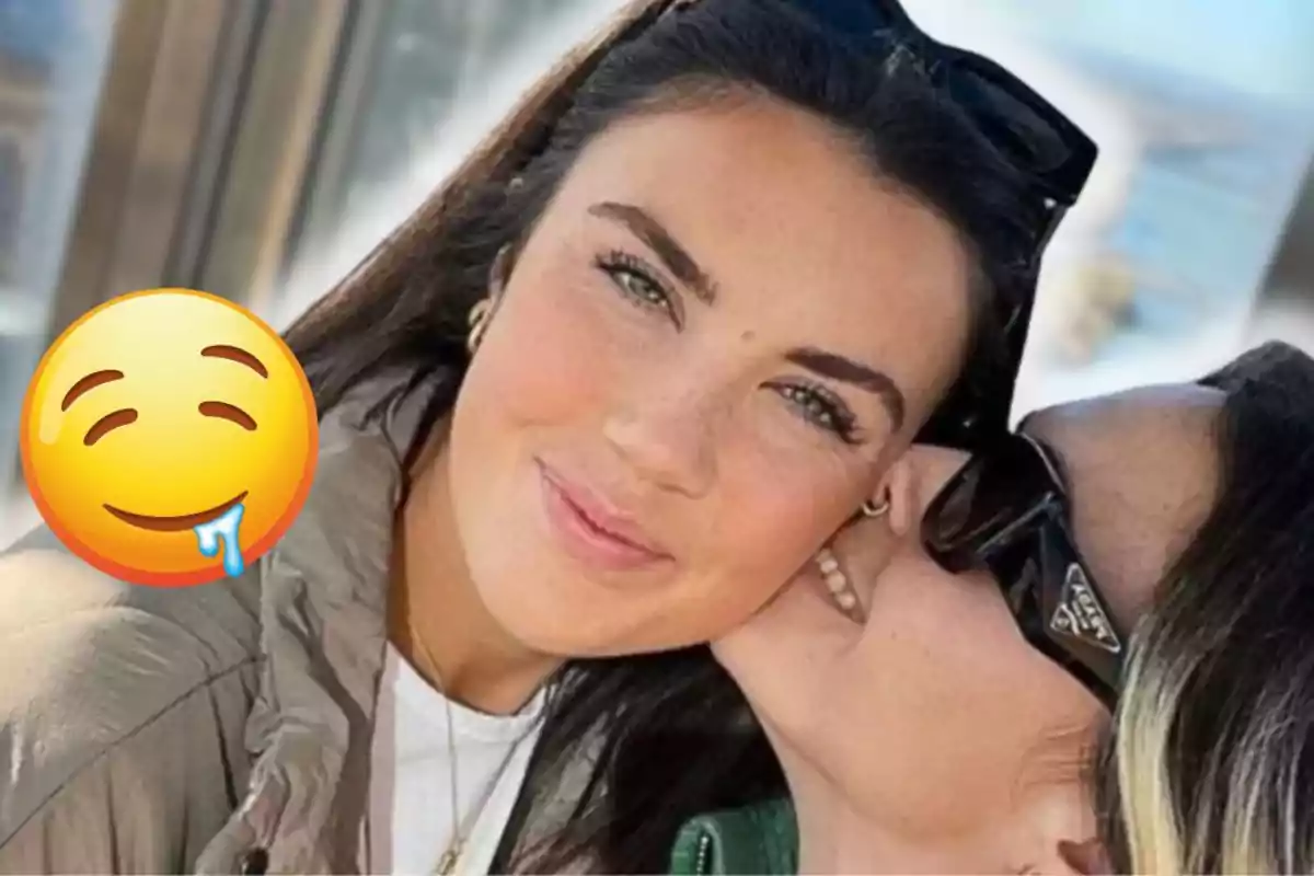 Two women pose together while one of them kisses the other on the cheek and a drooling smiley emoji covers part of the image.