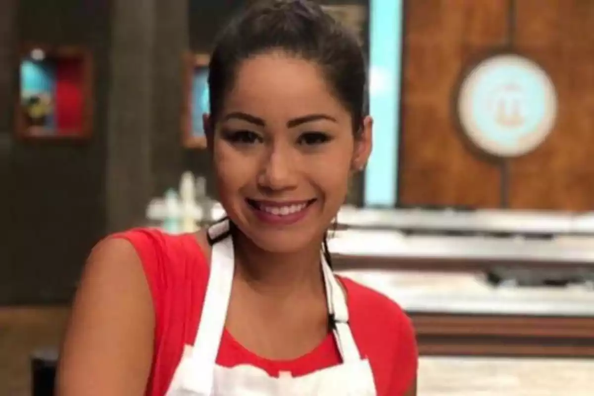 Yanin Campos con cabello recogido y camiseta roja sonríe mientras usa un mandil blanco en una cocina de concurso televisivo. Yanin Campos con cabello recogido y camiseta roja sonríe mientras usa un mandil blanco en una cocina de concurso televisivo.