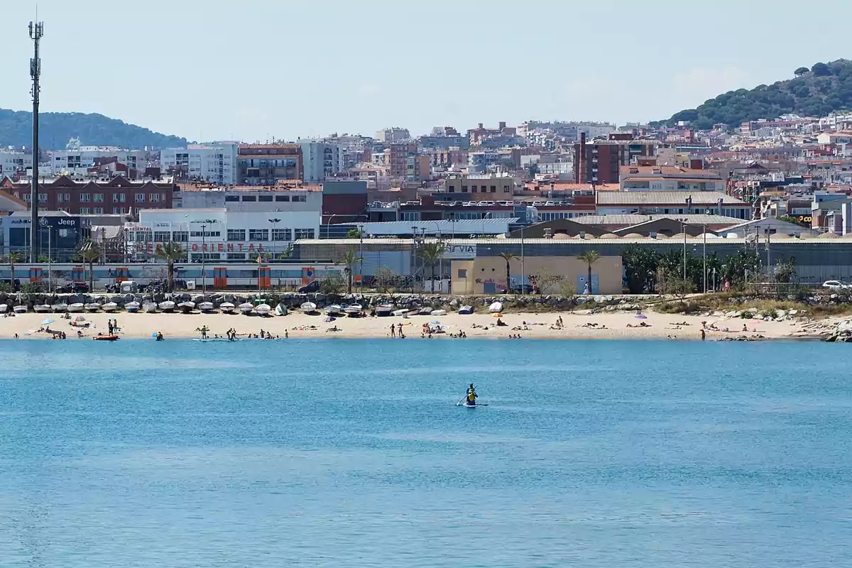 Playa urbana con sombrillas y personas disfrutando del sol y el mar, con edificios y colinas al fondo Playa urbana con sombrillas y personas disfrutando del sol y el mar, con edificios y colinas al fondo