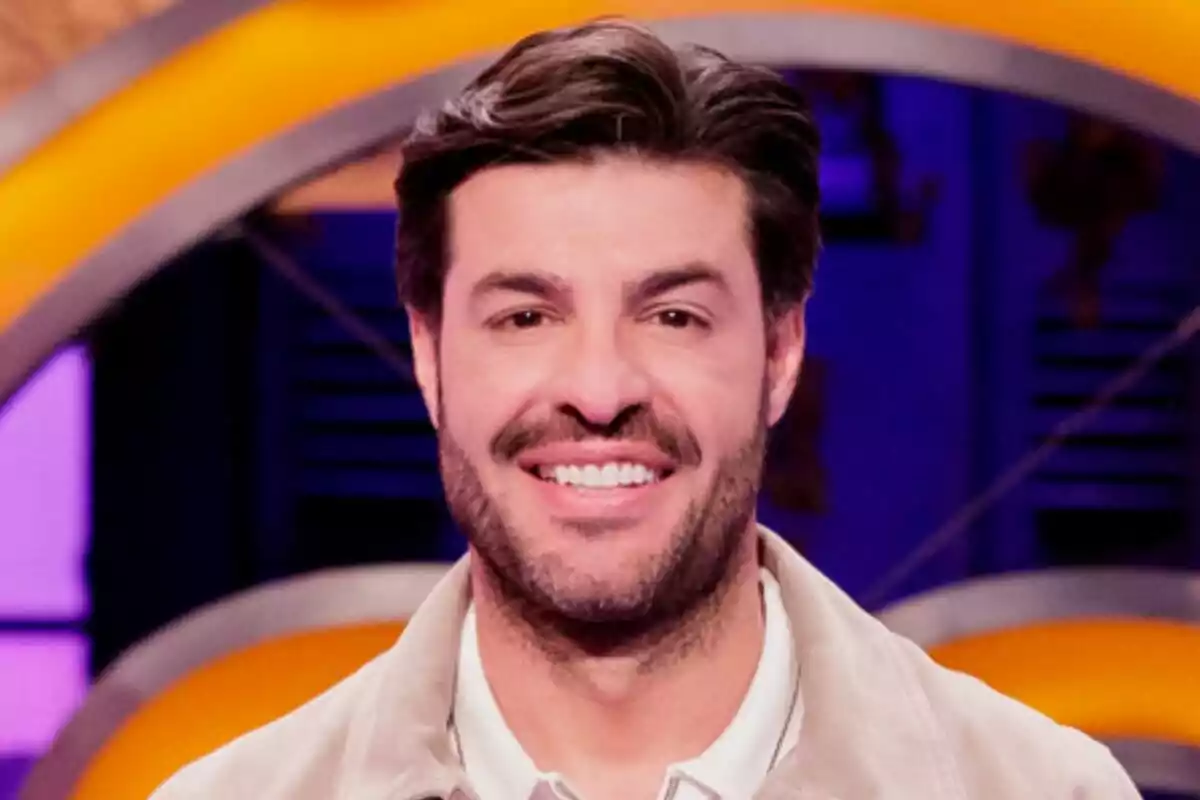 Miguel Torres joven de cabello oscuro y barba corta sonriendo frente a un fondo colorido en MasterChef Celebrity. Miguel Torres joven de cabello oscuro y barba corta sonriendo frente a un fondo colorido en MasterChef Celebrity.