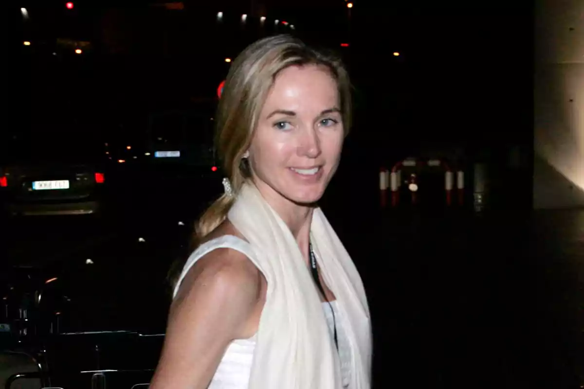 Miranda Rijnsburger con bufanda blanca y vestido claro sonriendo en un entorno nocturno urbano Miranda Rijnsburger con bufanda blanca y vestido claro sonriendo en un entorno nocturno urbano
