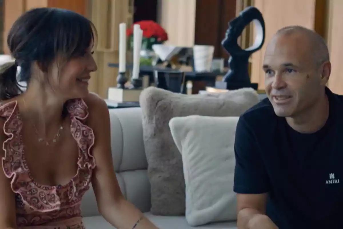Anna Ortiz y Andrés Iniesta conversan sonrientes sentados en un sofá en una sala decorada con cojines y objetos modernos. Captura de 'Mis Raíces' Anna Ortiz y Andrés Iniesta conversan sonrientes sentados en un sofá en una sala decorada con cojines y objetos modernos. Captura de 'Mis Raíces'