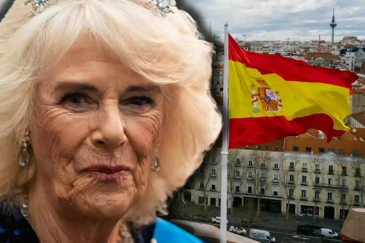 La reina Camila expressió seriosa en primer pla amb una corona, al fons una bandera d’Espanya onejant sobre una ciutat