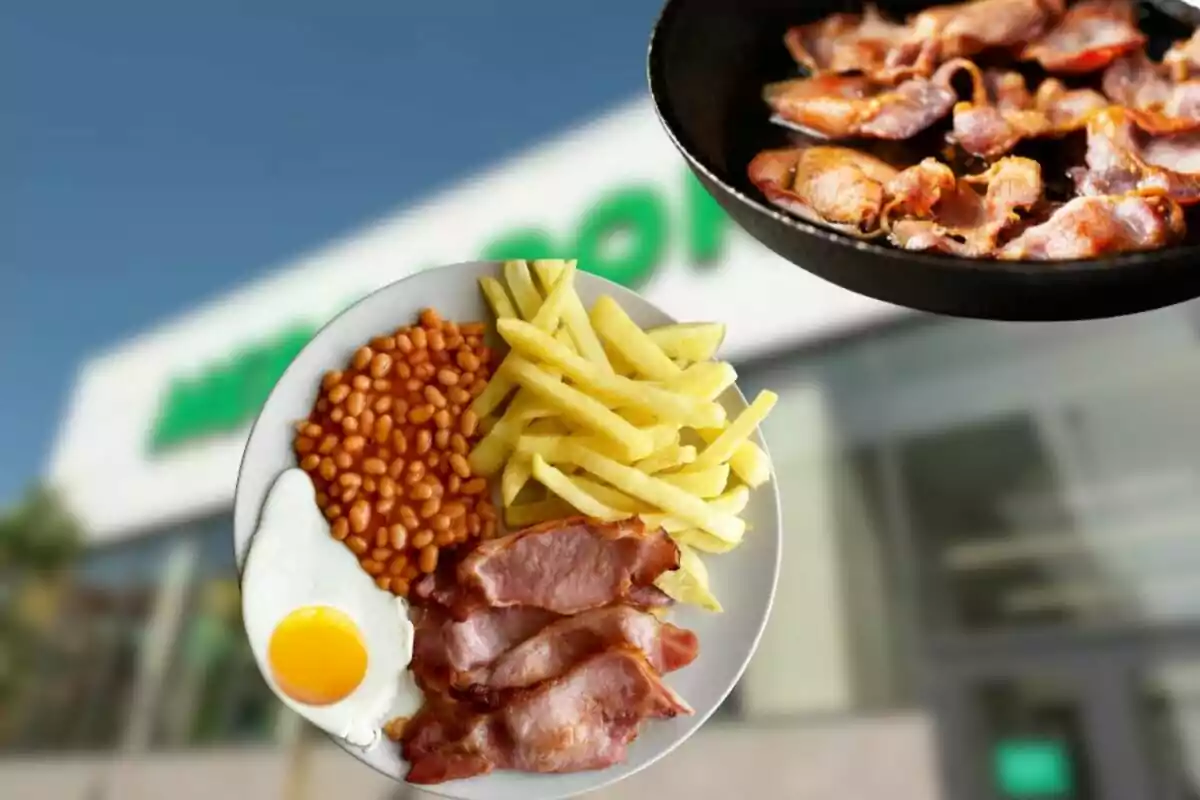 Un plato con papas fritas, frijoles, huevo frito y tocino frente a un edificio desenfocado, con una sartén llena de tocino en la esquina superior derecha Un plato con papas fritas, frijoles, huevo frito y tocino frente a un edificio desenfocado, con una sartén llena de tocino en la esquina superior derecha