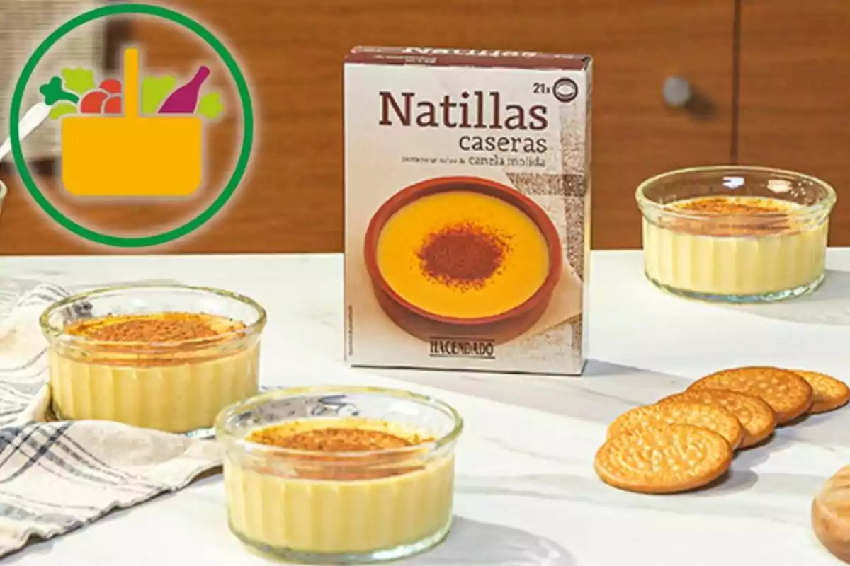 Postres de natilles casolanes en recipients de vidre al costat d’una capsa del producte i diverses galetes sobre una taula blanca Postres de natilles casolanes en recipients de vidre al costat d’una capsa del producte i diverses galetes sobre una taula blanca