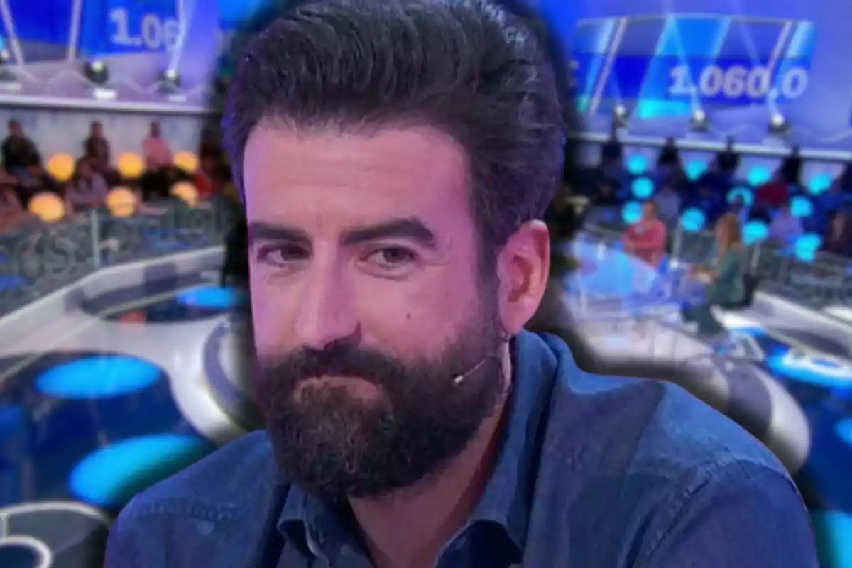 Rafa Castaño con micrófono en la mejilla sentado en un set de televisión con luces azules y público al fondo