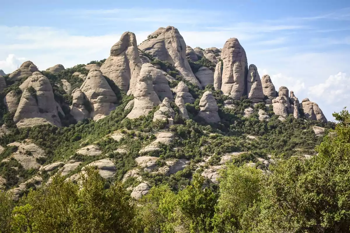 Formacions rocoses de Montserrat envoltades de vegetació sota un cel blau Formacions rocoses de Montserrat envoltades de vegetació sota un cel blau