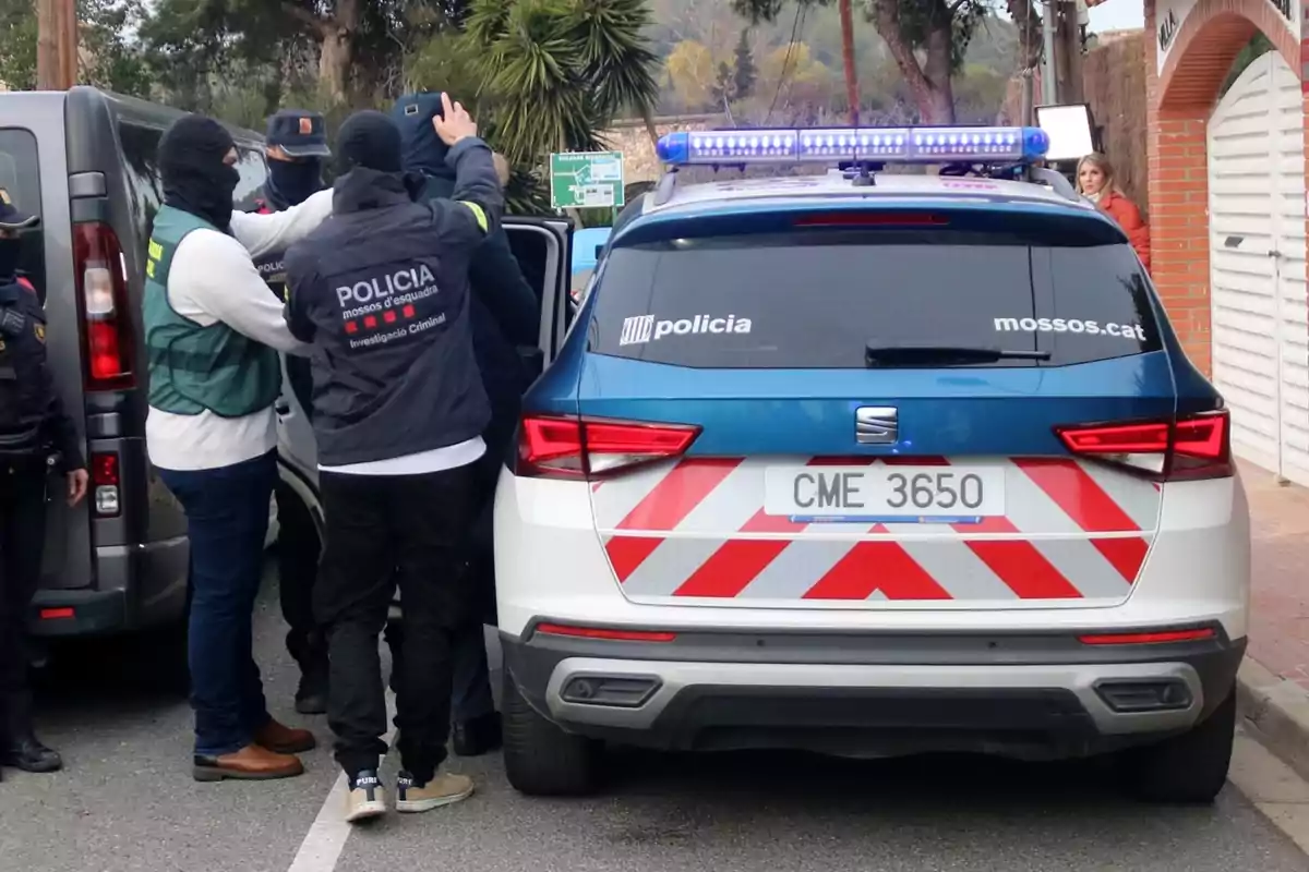 Diversos agents de policia detenen una persona al costat d’una patrulla dels Mossos d’Esquadra en un carrer residencial