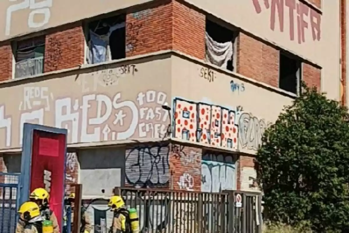 Bombers amb equip de protecció davant d’un edifici abandonat amb grafits i finestres trencades