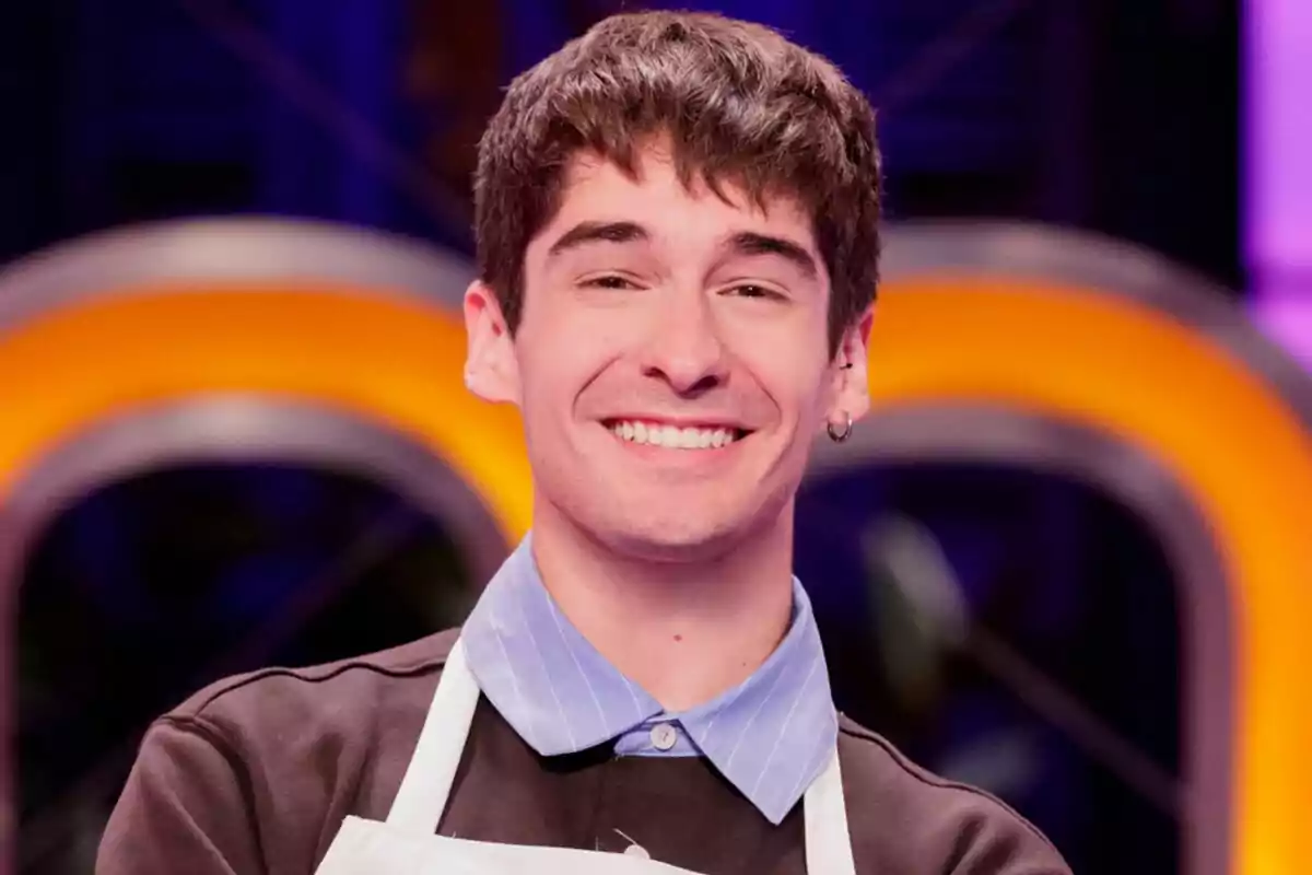 Necho Vidal somrient amb davantal blanc de MasterChef Celebrity i fons acolorit Necho Vidal somrient amb davantal blanc de MasterChef Celebrity i fons acolorit