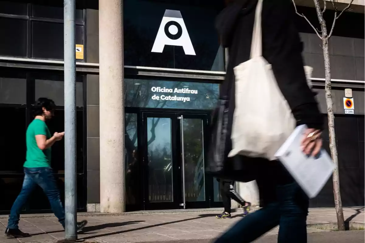 Persones caminant davant l’entrada de l’Oficina Antifrau de Catalunya en un dia assolellat