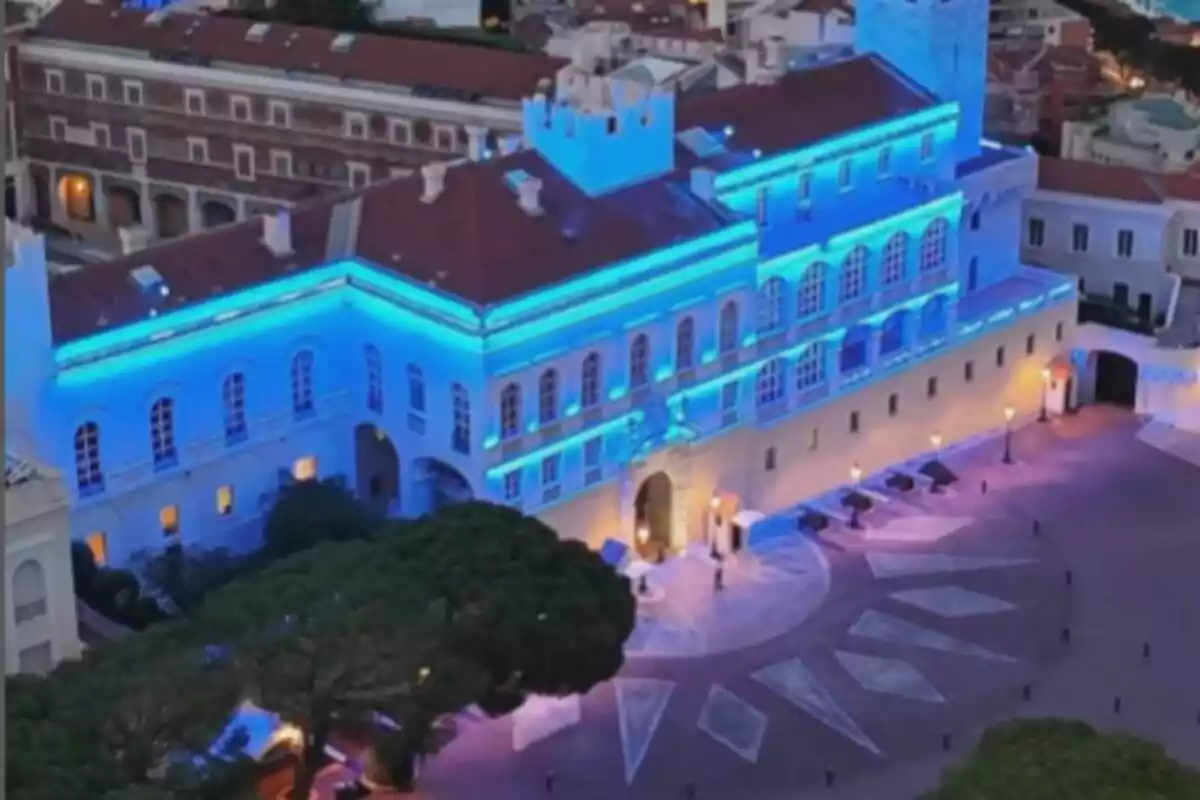 Edifici històric il·luminat amb llums blaves durant la nit, amb una plaça àmplia al davant i arbres al voltant. Edifici històric il·luminat amb llums blaves durant la nit, amb una plaça àmplia al davant i arbres al voltant.