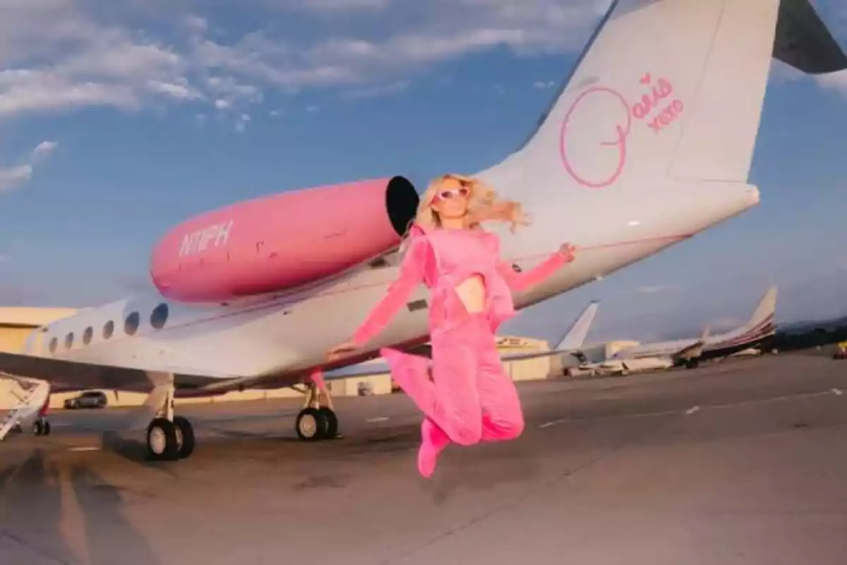 Mujer vestida de rosa saltando frente a un jet privado blanco y rosa en una pista de aeropuerto Mujer vestida de rosa saltando frente a un jet privado blanco y rosa en una pista de aeropuerto