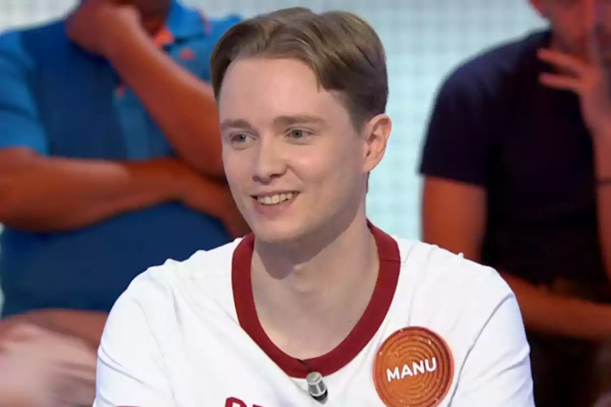 Manu sonriente con camiseta blanca y distintivo que dice Manu participando en un programa de televisión con personas sentadas al fondo. Captura de 'Pasapalabra' Manu sonriente con camiseta blanca y distintivo que dice Manu participando en un programa de televisión con personas sentadas al fondo. Captura de 'Pasapalabra'