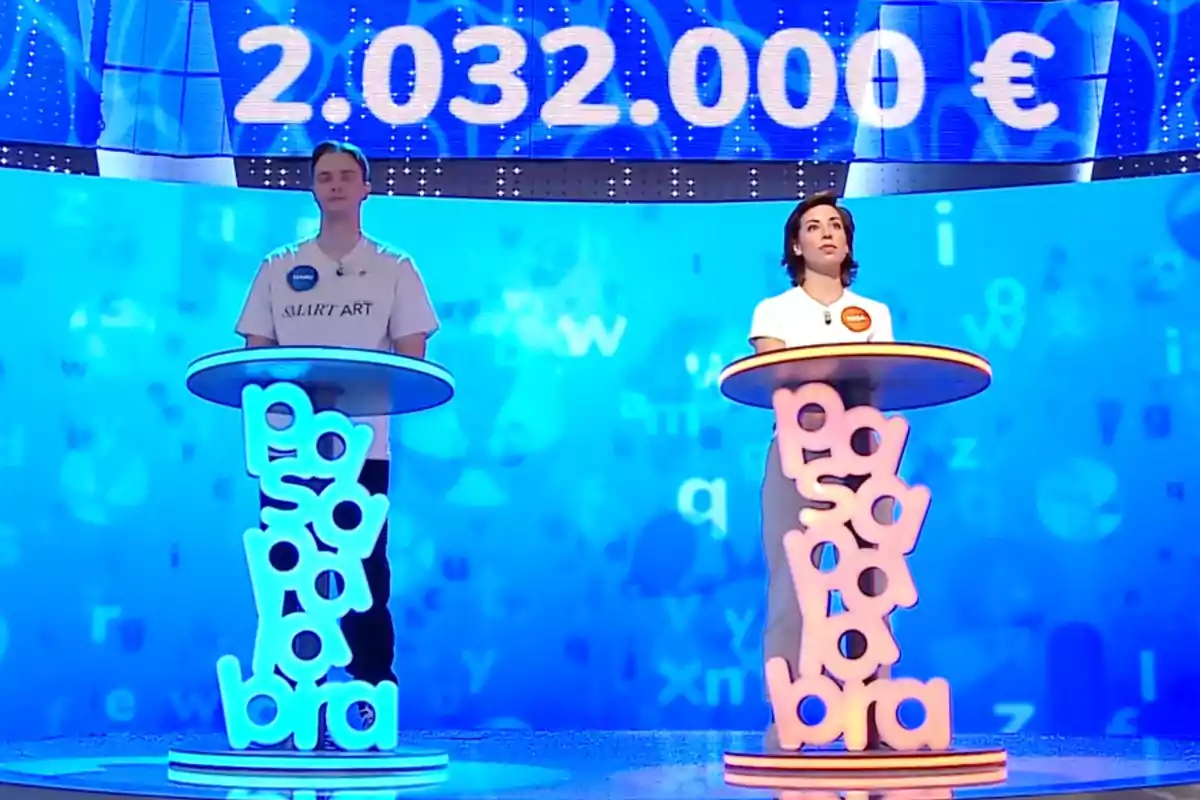 Manu i Rosa drets darrere de faristols il·luminats en un plató de televisió amb un fons blau i una xifra gran de diners en euros a la part superior. Captura de 'Pasapalabra' Manu i Rosa drets darrere de faristols il·luminats en un plató de televisió amb un fons blau i una xifra gran de diners en euros a la part superior. Captura de 'Pasapalabra'