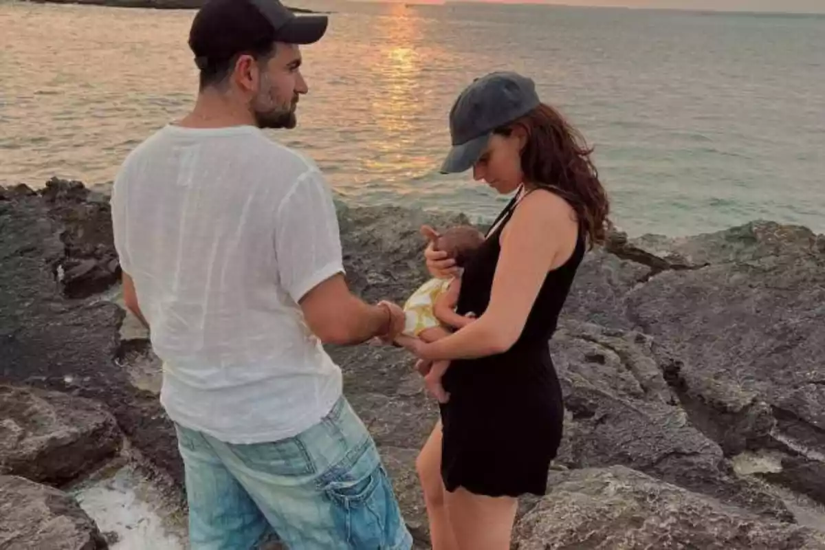 Pareja con un bebé en brazos disfrutando de un atardecer junto al mar sobre rocas Pareja con un bebé en brazos disfrutando de un atardecer junto al mar sobre rocas