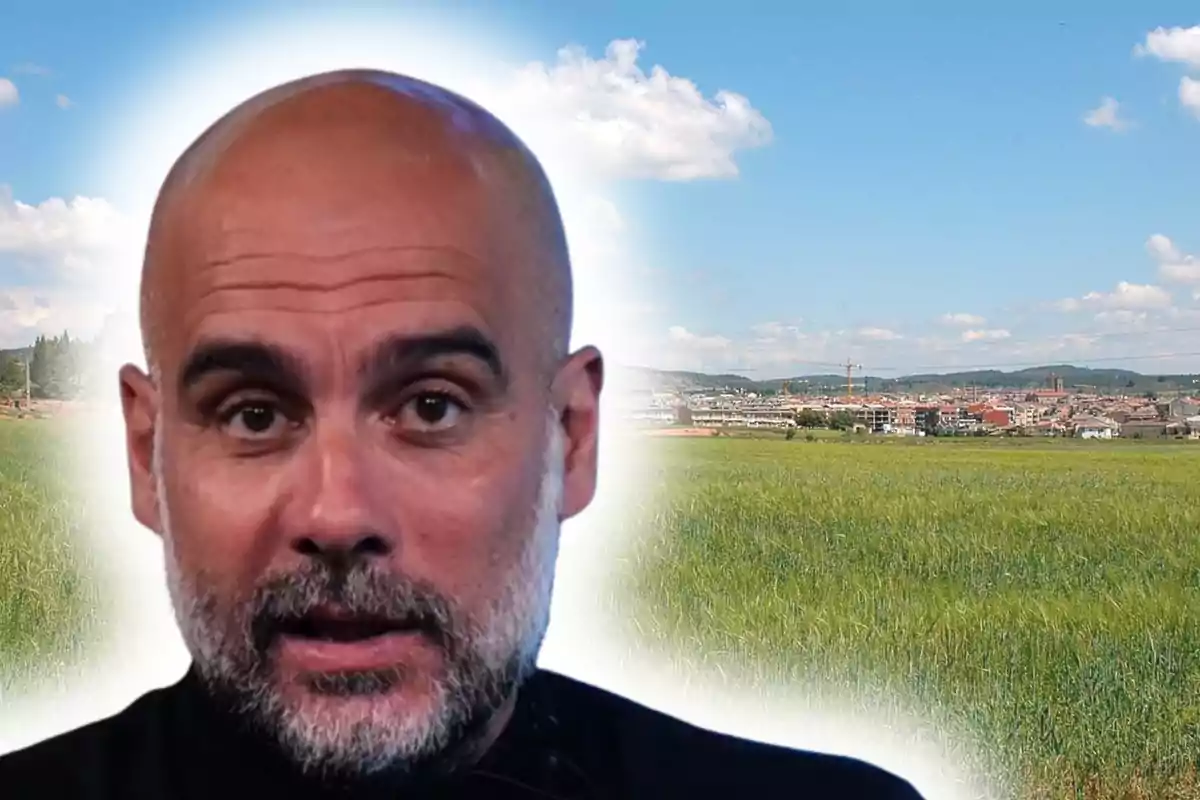Primer pla d’un home calb amb barba retallada sobre un fons de camp verd i cel blau amb núvols i una ciutat al fons