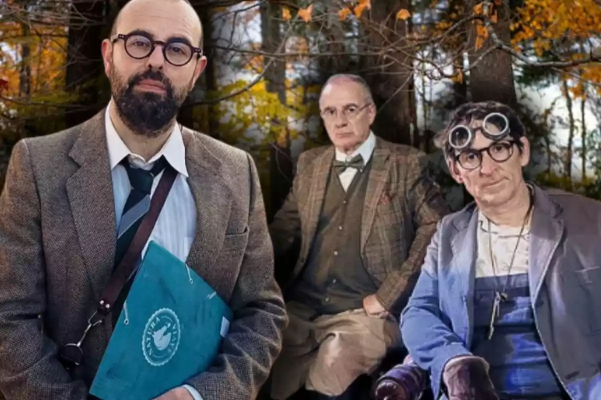 Tres hombres vestidos con ropa formal y de época posan en un bosque otoñal, uno de ellos sostiene una carpeta azul y otro lleva gafas de protección en la cabeza.