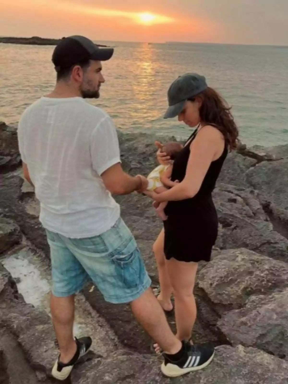 Alba Brunet i el seu marit amb un nadó en braços drets sobre roques vora el mar durant la posta de sol Alba Brunet i el seu marit amb un nadó en braços drets sobre roques vora el mar durant la posta de sol