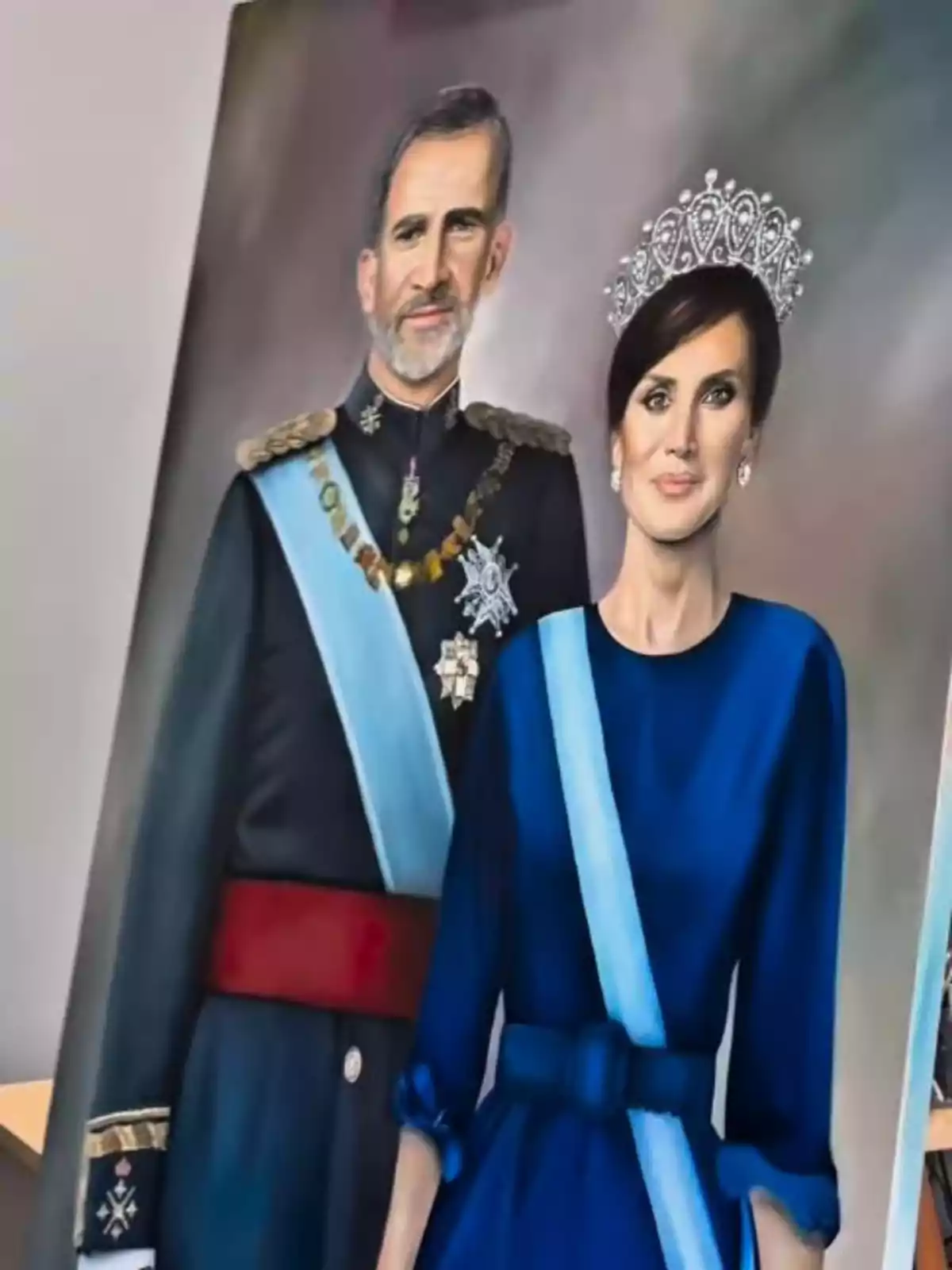 Painting of King Felipe VI and Queen Letizia in formal attire with blue sashes against a neutral background Painting of King Felipe VI and Queen Letizia in formal attire with blue sashes against a neutral background