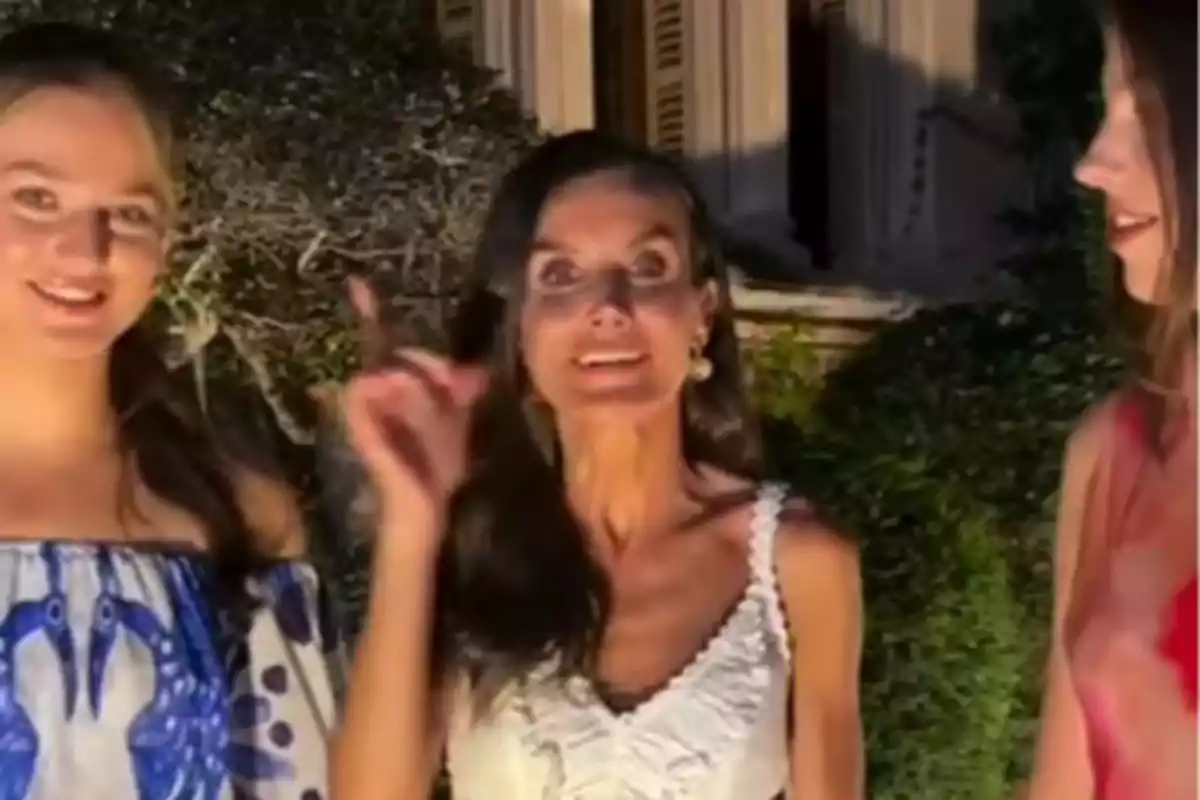 La princesa Leonor, la reina Letizia y la infanta Sofía posan al aire libre durante la noche con vegetación y un edificio de fondo La princesa Leonor, la reina Letizia y la infanta Sofía posan al aire libre durante la noche con vegetación y un edificio de fondo