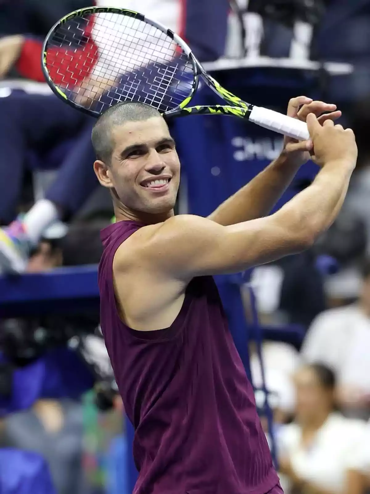 Carlos Alcaraz smiling, celebrating on the court with a racket in his hand and a sleeveless burgundy jersey Carlos Alcaraz smiling, celebrating on the court with a racket in his hand and a sleeveless burgundy jersey