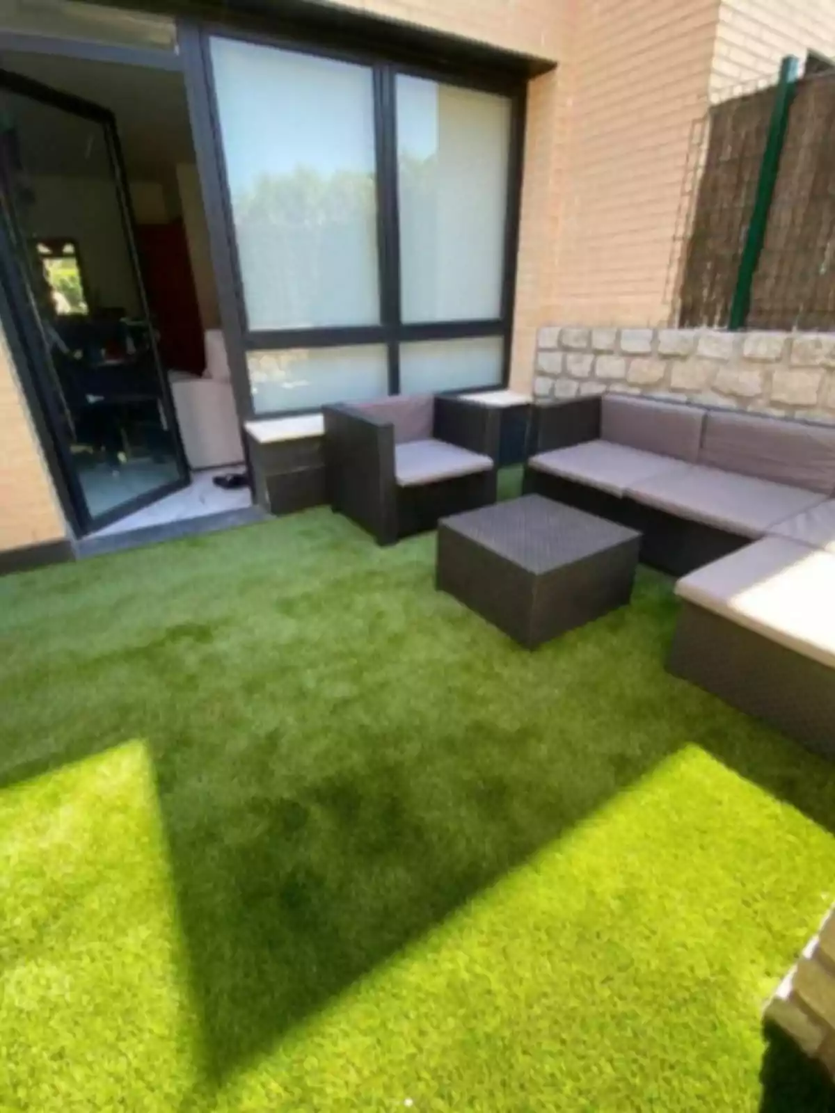 Terrassa amb gespa artificial i mobles de jardí al costat d’una paret de maó i una porta de vidre Terrassa amb gespa artificial i mobles de jardí al costat d’una paret de maó i una porta de vidre