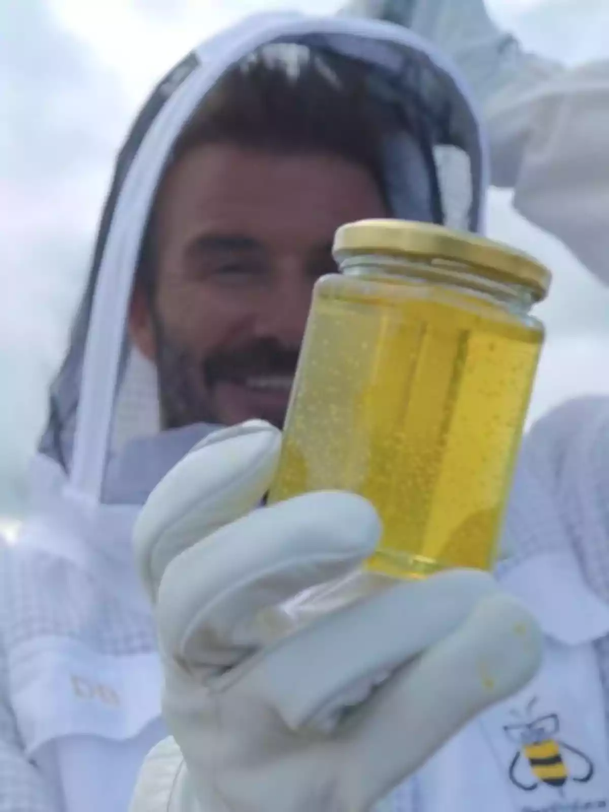 David Beckham amb vestit d’apicultor sostenint un pot de mel davant de la càmera David Beckham amb vestit d’apicultor sostenint un pot de mel davant de la càmera