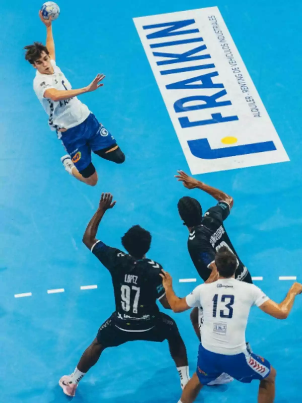 Pablo Urdangarin con uniforme blanco y azul salta para lanzar el balón mientras tres rivales intentan bloquearlo en una cancha azul Pablo Urdangarin con uniforme blanco y azul salta para lanzar el balón mientras tres rivales intentan bloquearlo en una cancha azul