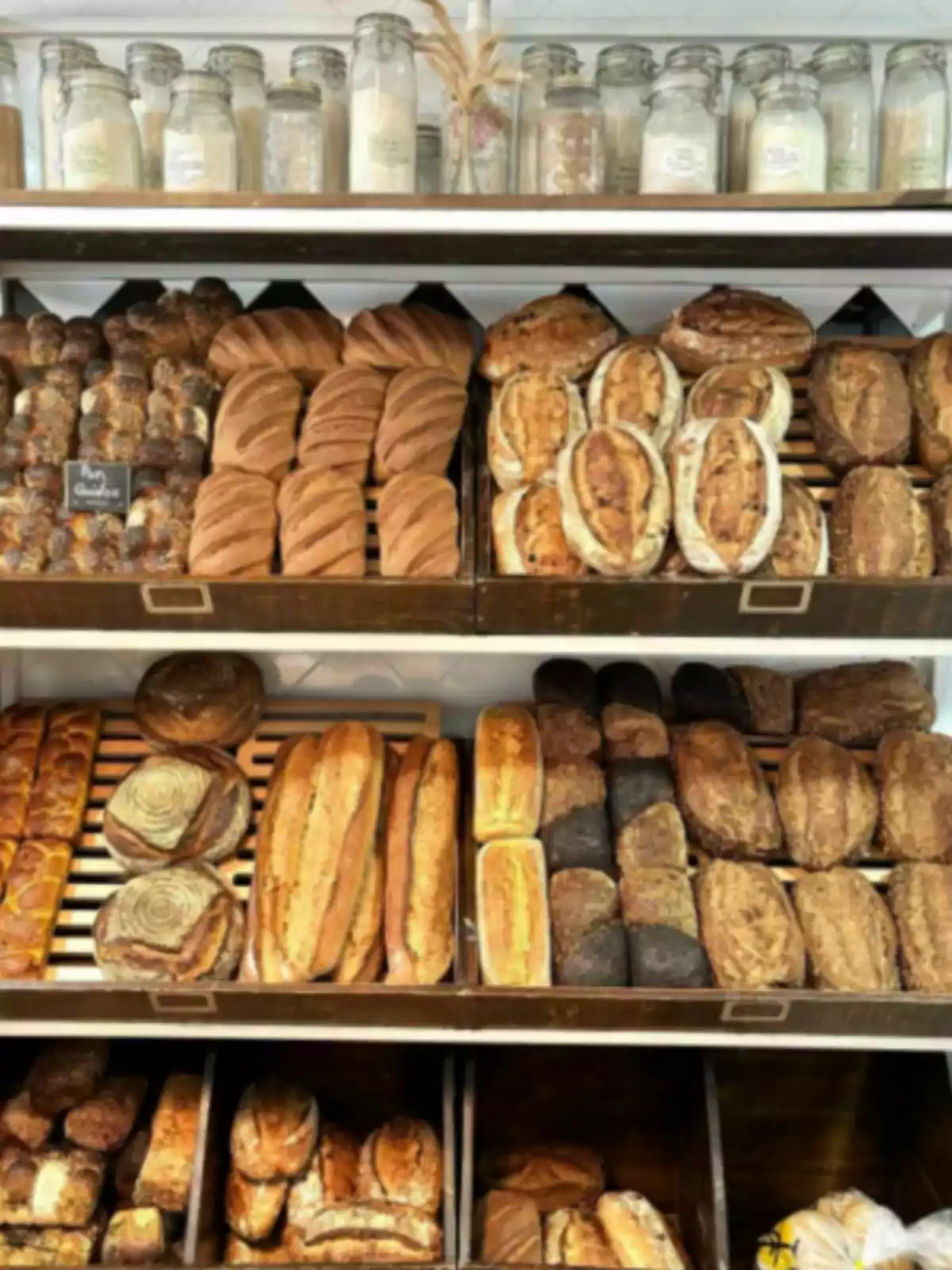 Bakery shelf with different types of craft-made breads organized on trays and jars of ingredients on the top. Bakery shelf with different types of craft-made breads organized on trays and jars of ingredients on the top.