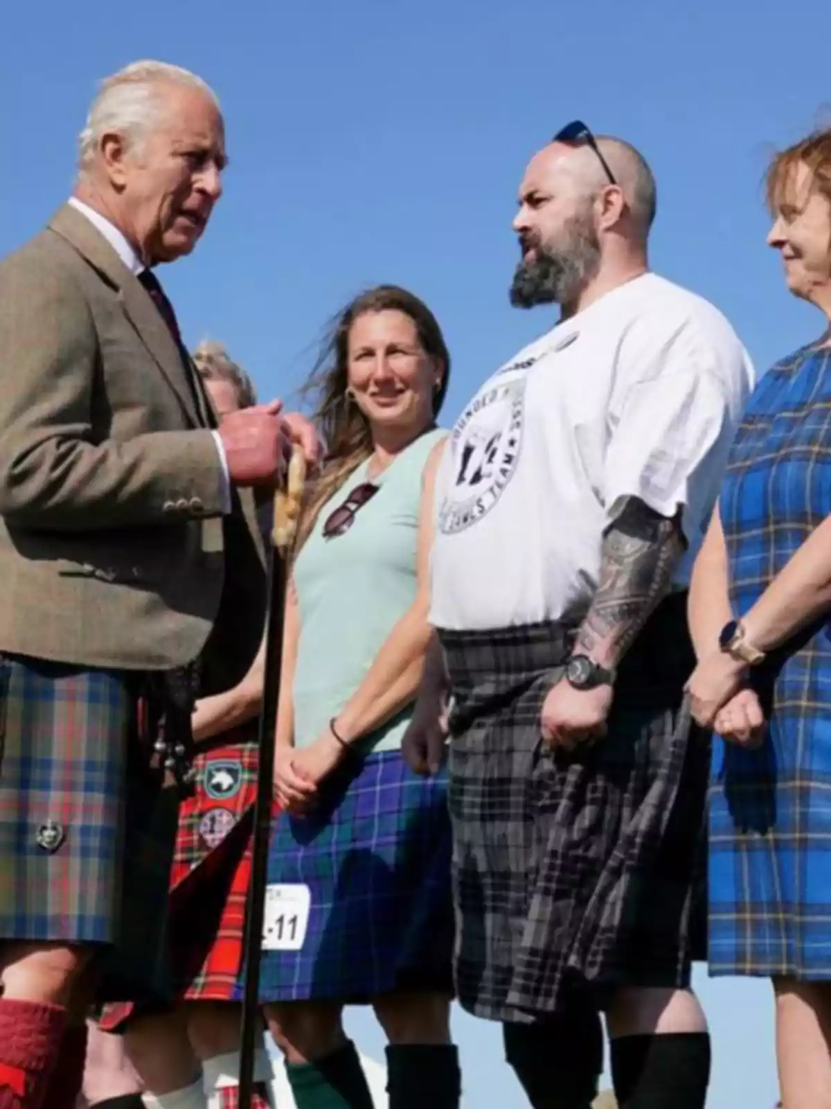 A group of people dressed in kilts is talking outdoors under a clear sky. A group of people dressed in kilts is talking outdoors under a clear sky.