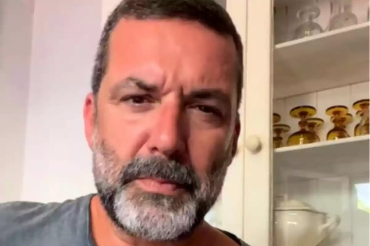 Jaime Anglada amb expressió seriosa davant d’un moble amb copes i recipients de vidre grocs Jaime Anglada amb expressió seriosa davant d’un moble amb copes i recipients de vidre grocs