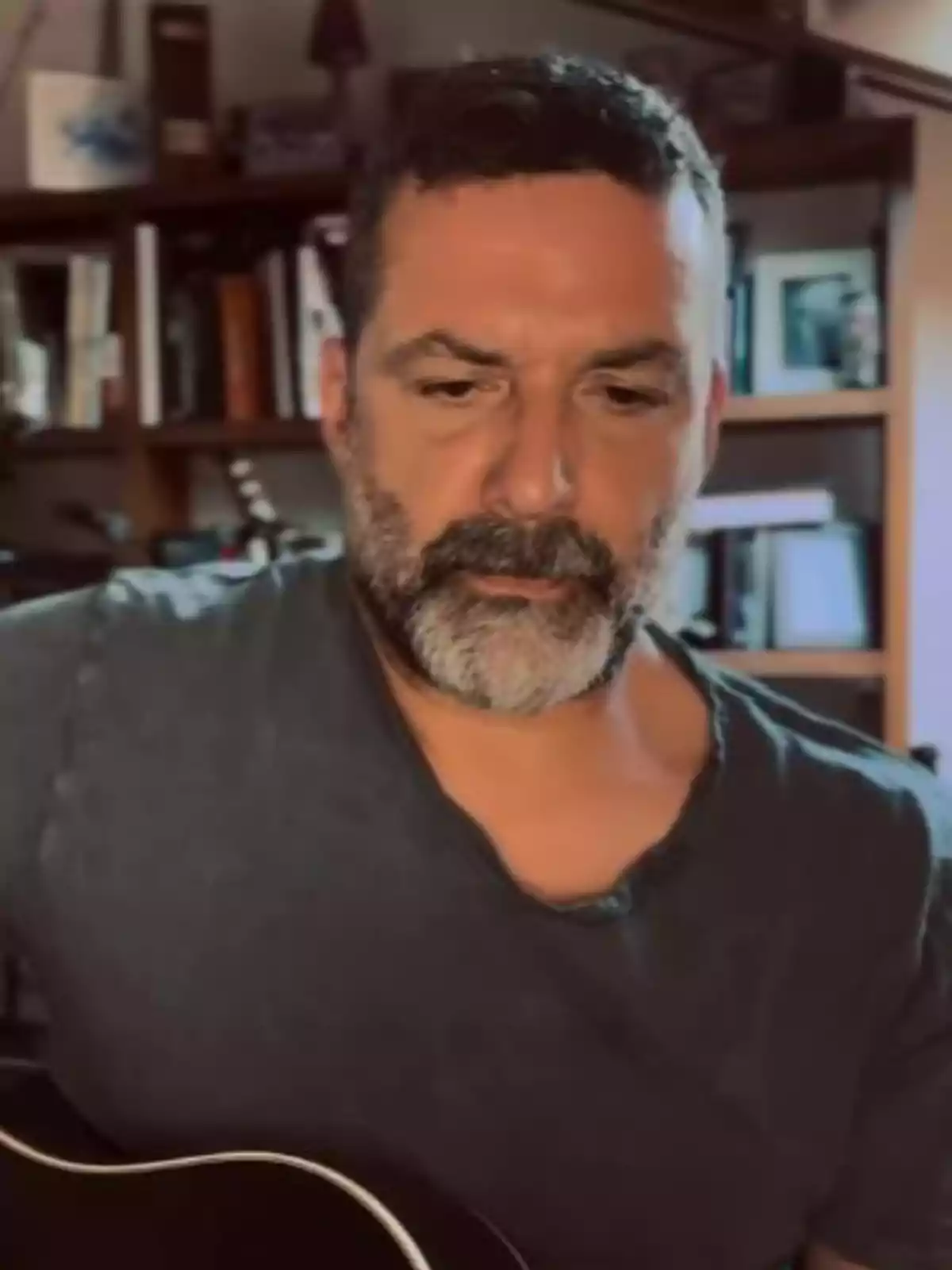 Jaime Anglada tocant una guitarra en una habitació amb prestatgeria de fons Jaime Anglada tocant una guitarra en una habitació amb prestatgeria de fons