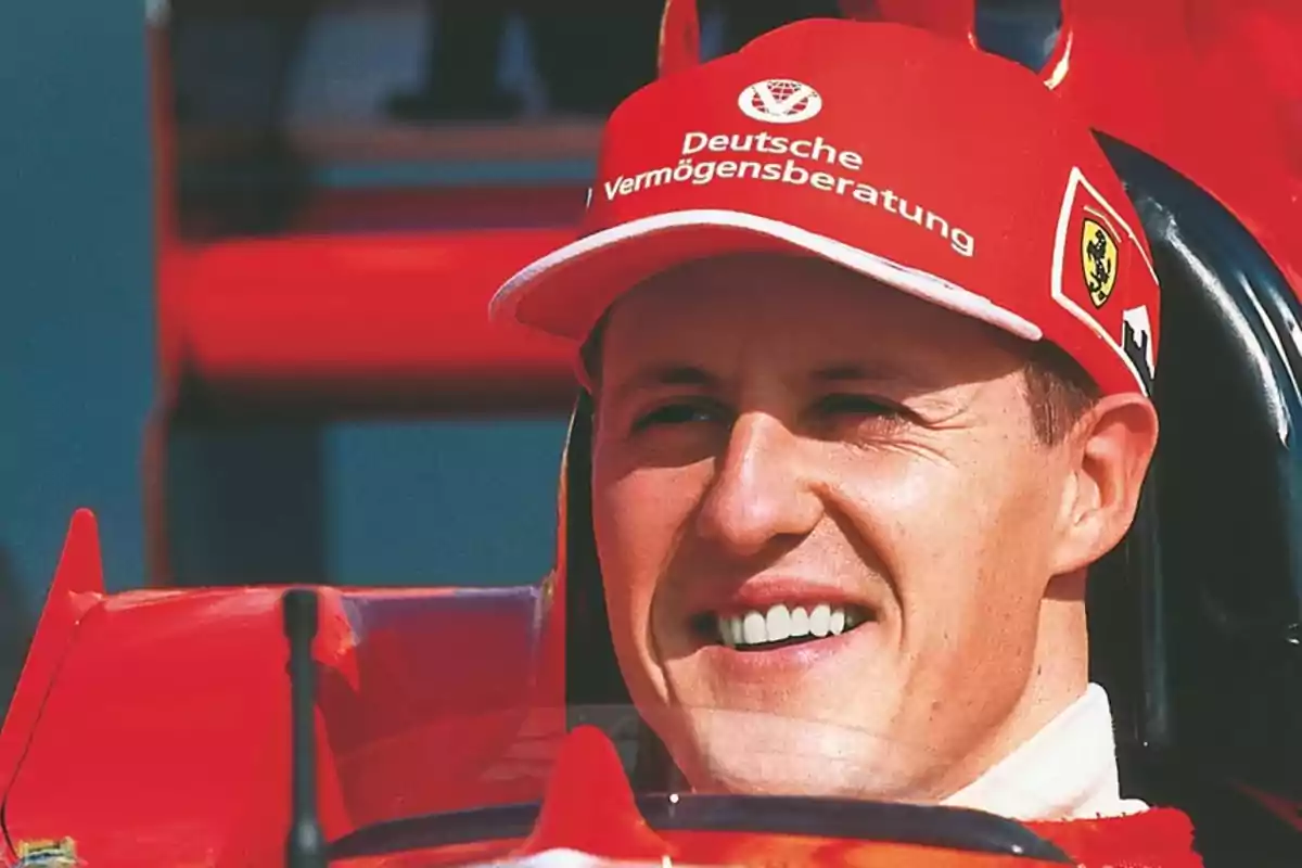 Michael Schumacher amb gorra vermella i uniforme de Ferrari somrient dins d’un monoplaça Michael Schumacher amb gorra vermella i uniforme de Ferrari somrient dins d’un monoplaça