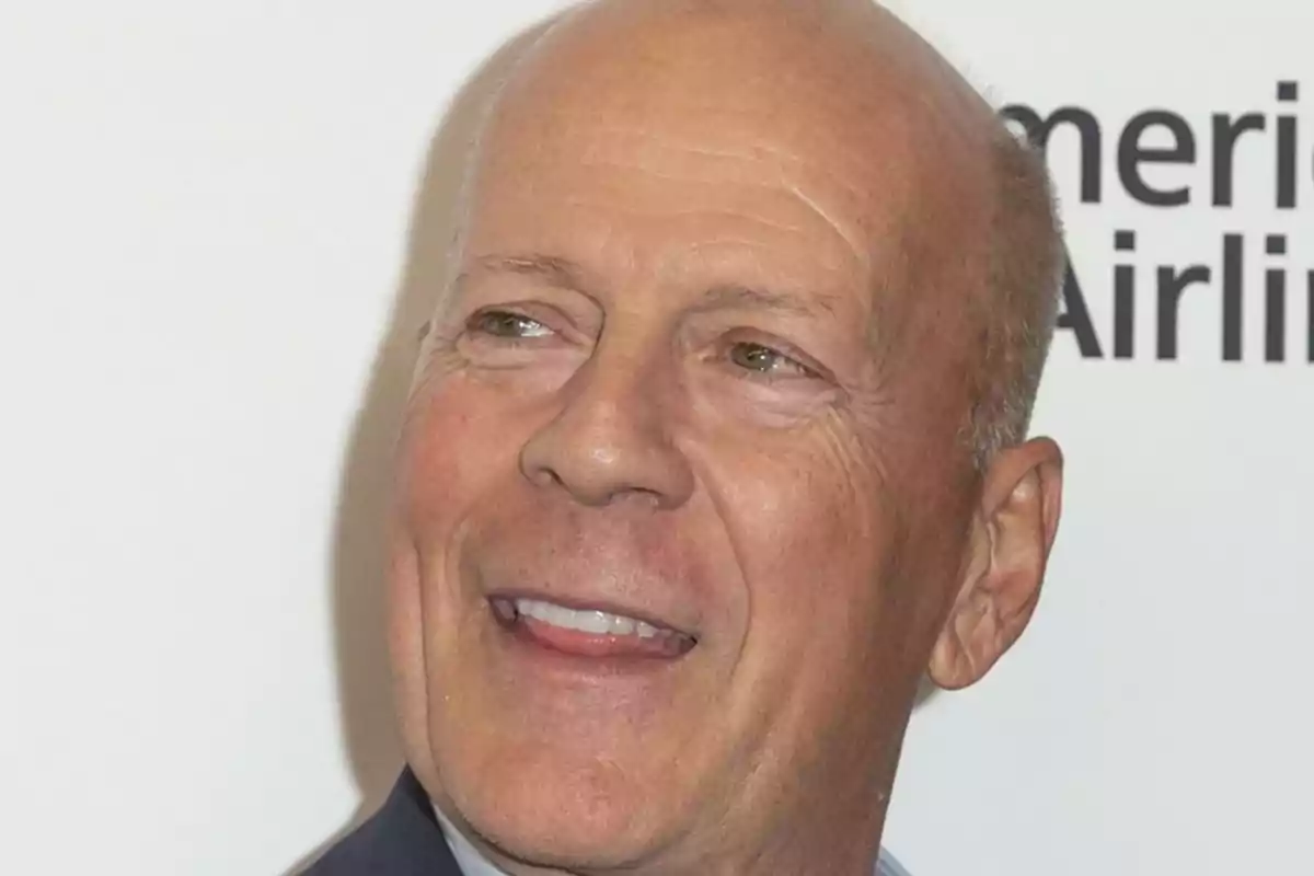 Bruce Willis smiling and looking to the side with a white background and partially visible black letters Bruce Willis smiling and looking to the side with a white background and partially visible black letters