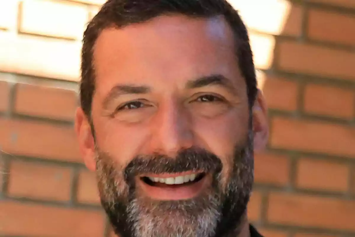Primer pla de Jaime Anglada amb barba i cabell curt somrient davant d’una paret de maons. Primer pla de Jaime Anglada amb barba i cabell curt somrient davant d’una paret de maons.